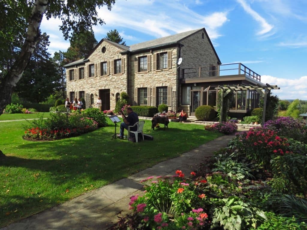 Front of the 1962 Georgian stone house at Sherwood Farm with flower beds and lawn